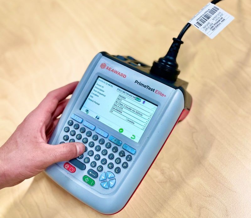 Test and Tag technician using portable appliance tester for inspecting an electrical lead with safety tags and labels attached, ensuring equipment compliance and safety.